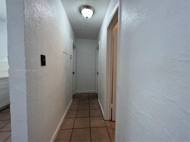 corridor featuring a textured wall and light tile patterned floors