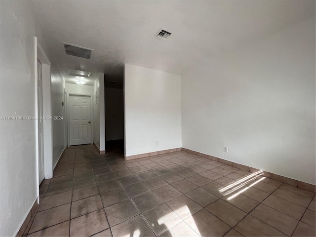 empty room featuring dark tile patterned flooring, baseboards, and visible vents