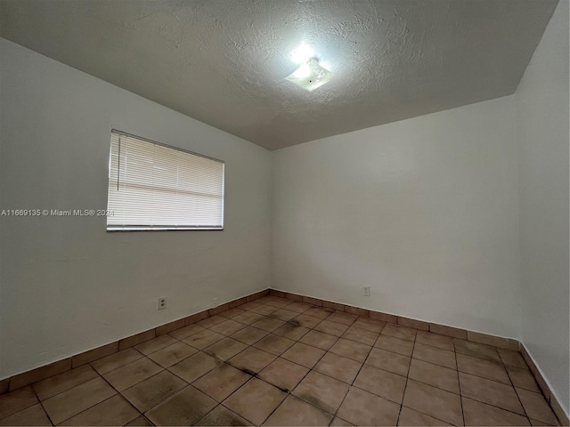 spare room featuring baseboards, a textured ceiling, and light tile patterned flooring