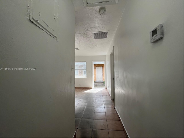 corridor with dark tile patterned floors, a textured ceiling, visible vents, and baseboards
