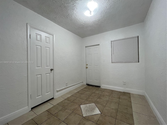 tiled spare room featuring baseboards, a textured wall, and a textured ceiling