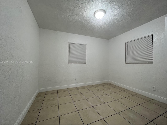 unfurnished room with baseboards, a textured ceiling, a textured wall, and light tile patterned floors