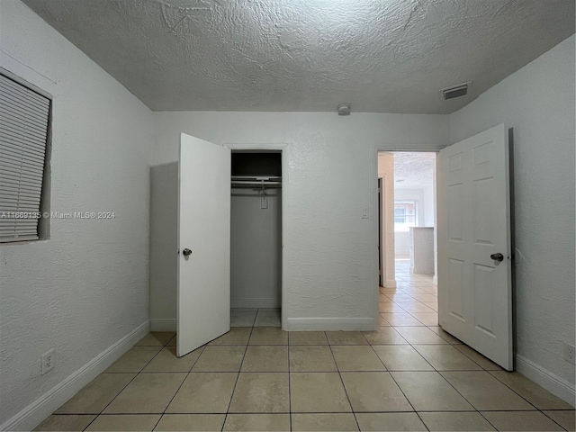 unfurnished bedroom featuring a textured ceiling, light tile patterned floors, baseboards, a closet, and a textured wall