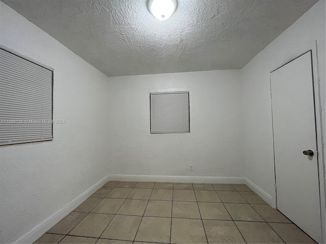 spare room featuring baseboards, a textured ceiling, and light tile patterned floors