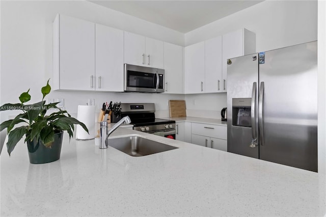 kitchen with appliances with stainless steel finishes, sink, light stone counters, and white cabinets