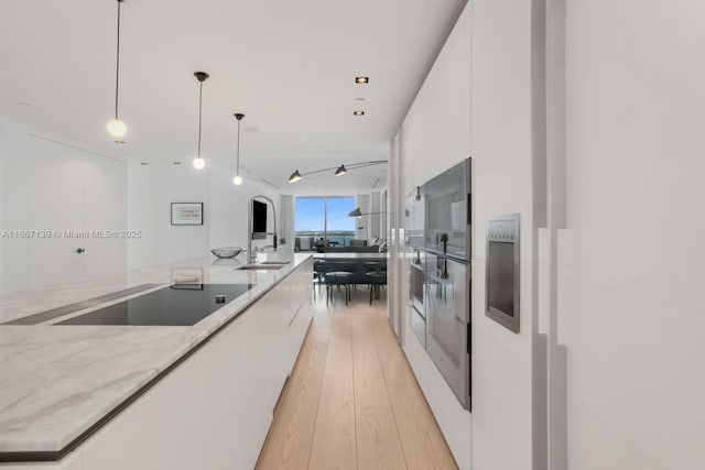 kitchen with light stone countertops, white cabinets, decorative light fixtures, light hardwood / wood-style floors, and sink