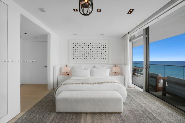 bedroom featuring light wood-type flooring, a wall of windows, a water view, and access to outside