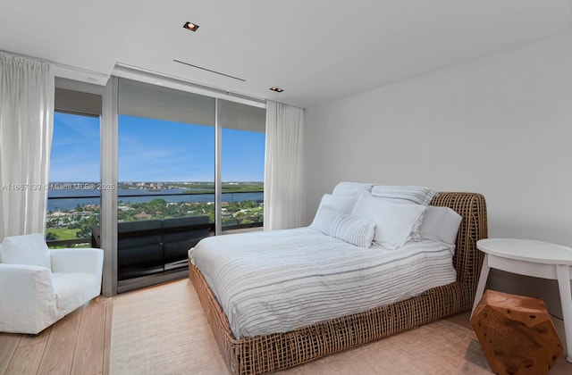 bedroom with a water view, expansive windows, and light hardwood / wood-style flooring