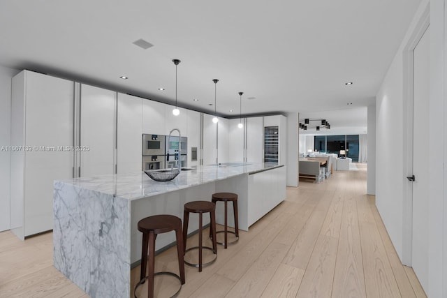 kitchen with white cabinets, light stone counters, a large island, and pendant lighting