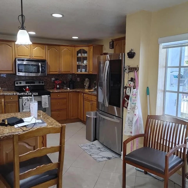 kitchen with light stone counters, hanging light fixtures, light tile patterned floors, backsplash, and appliances with stainless steel finishes