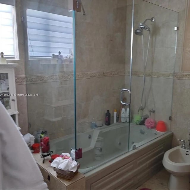 bathroom with tile walls, bath / shower combo with glass door, and a bidet