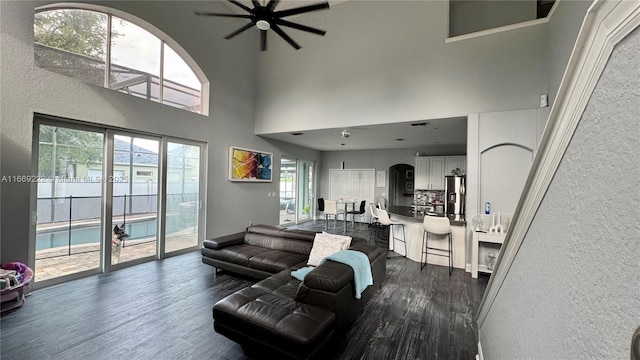 living room featuring ceiling fan, a towering ceiling, and dark wood-type flooring