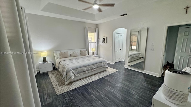 bedroom with dark hardwood / wood-style flooring, a tray ceiling, and ceiling fan