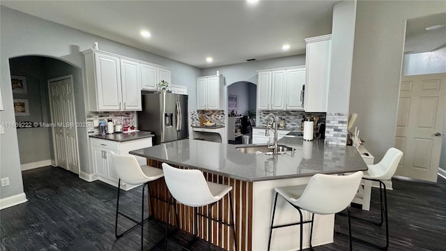 kitchen with a breakfast bar, white cabinets, sink, stainless steel fridge, and kitchen peninsula