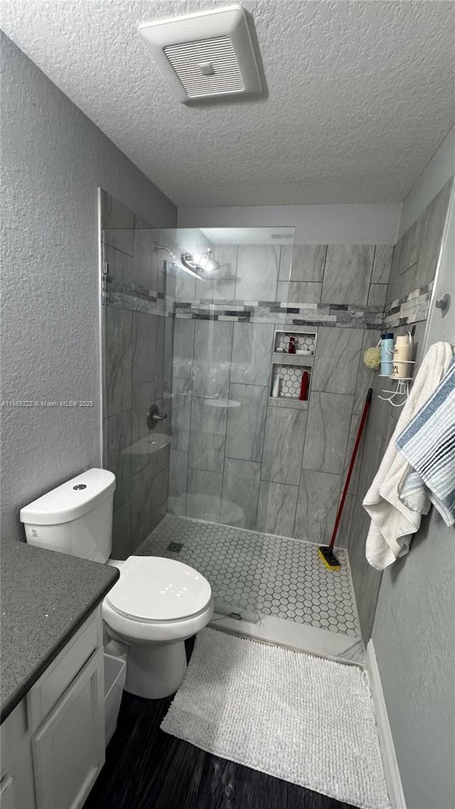 bathroom with a tile shower, vanity, a textured ceiling, and toilet