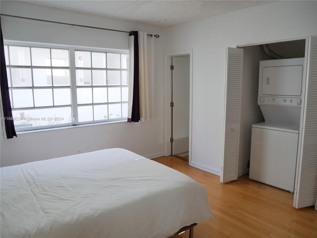 bedroom featuring a textured ceiling, stacked washer and clothes dryer, and light hardwood / wood-style flooring