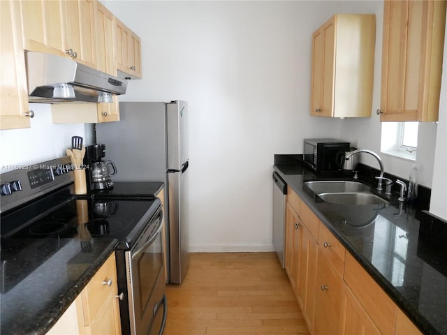 kitchen with dark stone countertops, appliances with stainless steel finishes, sink, and light hardwood / wood-style flooring