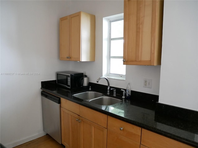 kitchen featuring dark stone countertops, dishwasher, and sink