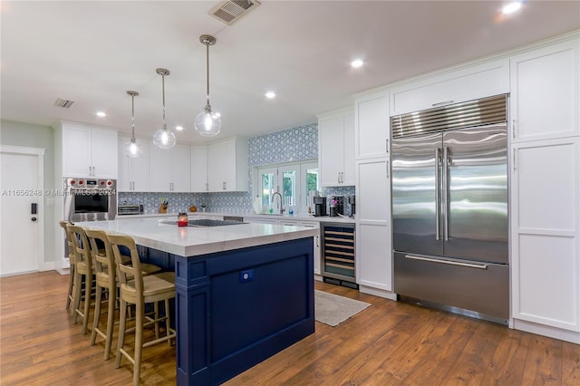 kitchen featuring white cabinetry, wine cooler, hanging light fixtures, a center island, and stainless steel appliances