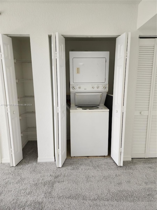 clothes washing area with light colored carpet and stacked washer / dryer