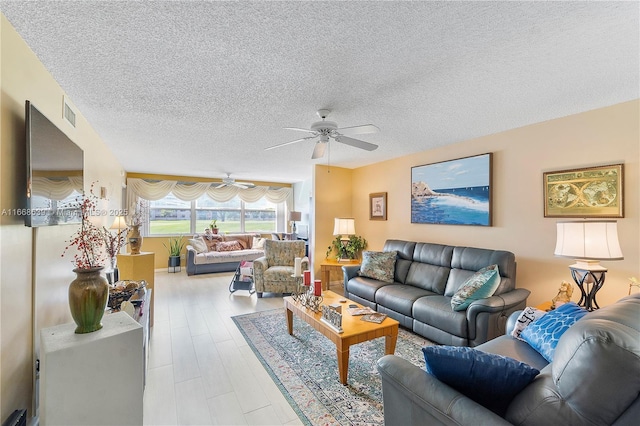 living room featuring light wood-type flooring, a textured ceiling, and ceiling fan