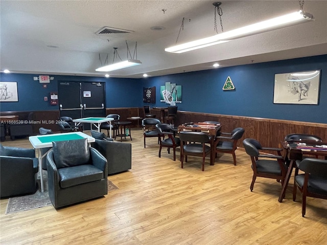 game room with wooden walls, light hardwood / wood-style flooring, and a textured ceiling