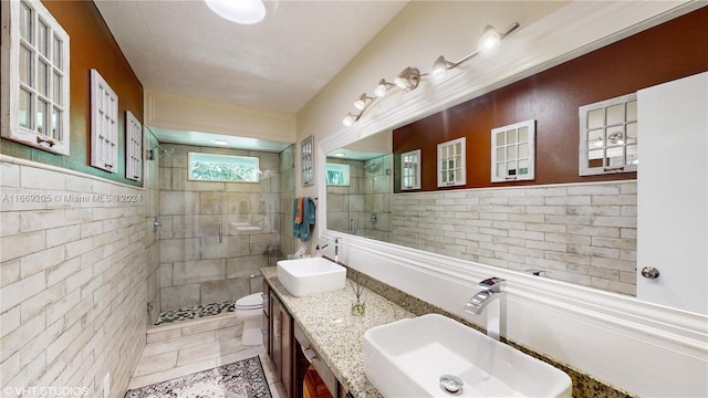 bathroom with vanity, toilet, a textured ceiling, walk in shower, and tile walls