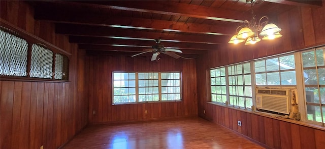 spare room featuring wood-type flooring, wooden walls, ceiling fan with notable chandelier, and a healthy amount of sunlight