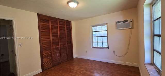 unfurnished bedroom with a wall unit AC, a closet, and dark wood-type flooring