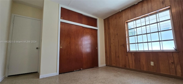 unfurnished bedroom with wooden walls, a closet, and multiple windows