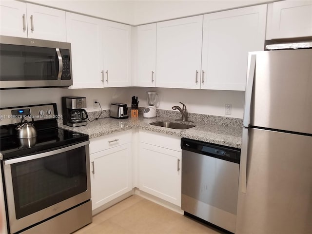 kitchen with light stone countertops, stainless steel appliances, white cabinetry, and sink