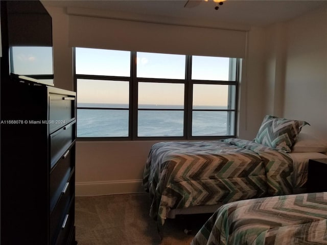 bedroom with dark carpet, a water view, and ceiling fan