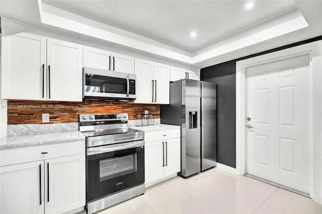 kitchen with white cabinets, appliances with stainless steel finishes, a tray ceiling, and tasteful backsplash