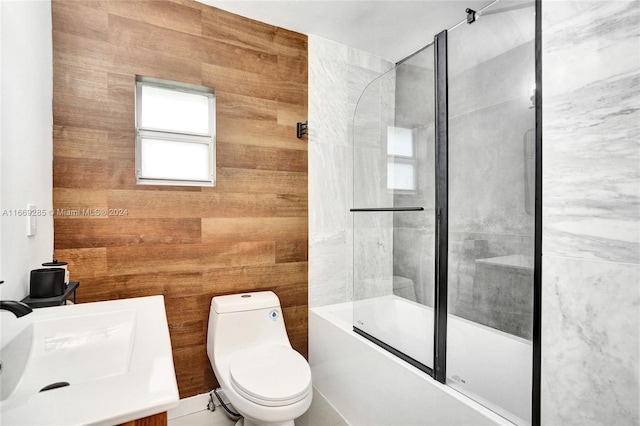 full bathroom featuring wood walls, shower / bath combination with glass door, vanity, and toilet