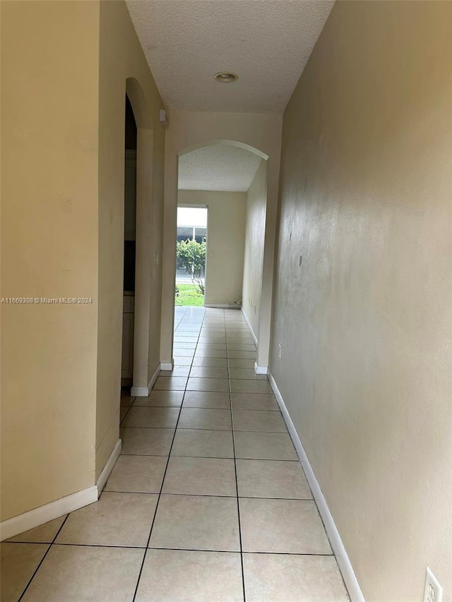 hall with a textured ceiling and light tile patterned floors