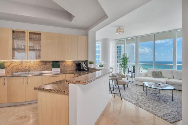 kitchen with sink, decorative backsplash, a water view, light brown cabinets, and dark stone countertops