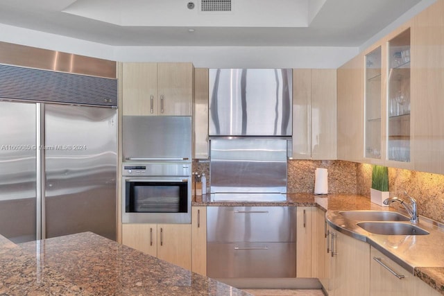 kitchen with stainless steel appliances, a raised ceiling, light brown cabinets, and sink