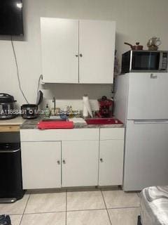 kitchen with light tile patterned flooring, white cabinetry, and white fridge