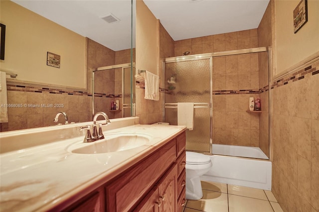 full bathroom with shower / bath combination with glass door, tile walls, tile patterned flooring, vanity, and toilet