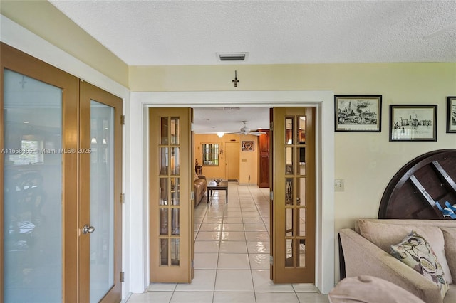 hallway with french doors, a textured ceiling, and light tile patterned floors