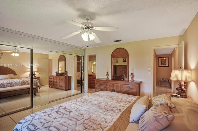 tiled bedroom with ceiling fan, two closets, and a textured ceiling