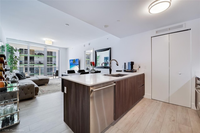 kitchen with stainless steel dishwasher, a sink, light countertops, open floor plan, and light wood-style flooring