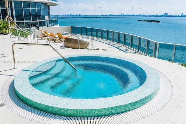 view of pool featuring a water view, a patio area, and an in ground hot tub