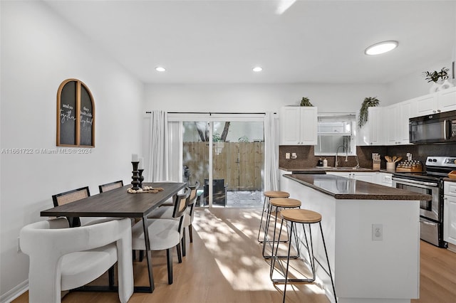 kitchen featuring a kitchen breakfast bar, black microwave, stainless steel electric range oven, white cabinets, and light wood finished floors