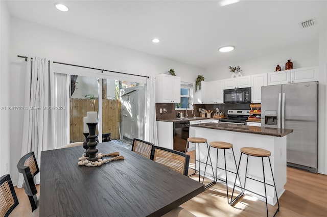 kitchen featuring black appliances, a center island, tasteful backsplash, light hardwood / wood-style floors, and white cabinetry