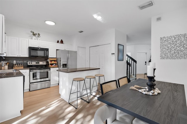 kitchen featuring a kitchen island, decorative backsplash, white cabinets, light hardwood / wood-style floors, and appliances with stainless steel finishes