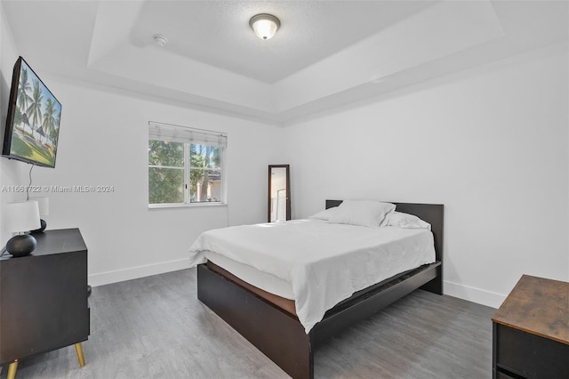 bedroom featuring baseboards, wood finished floors, and a tray ceiling