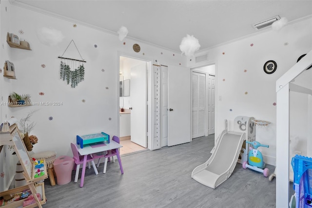 recreation room featuring crown molding, wood finished floors, and visible vents