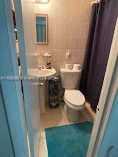 bathroom with tile walls, sink, tile patterned floors, curtained shower, and toilet