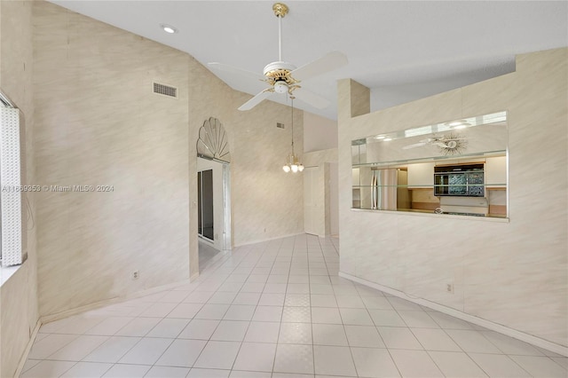 tiled empty room featuring ceiling fan with notable chandelier and high vaulted ceiling